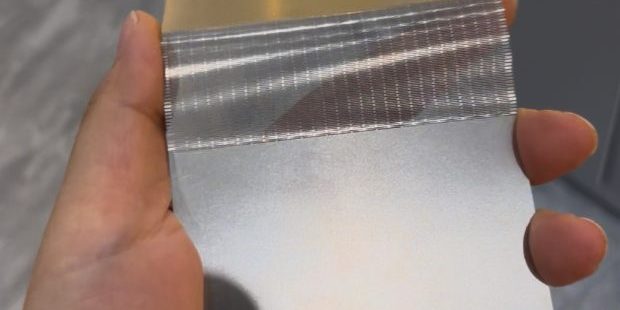 Handheld thin etched metal folding sample showing a dense precision flexible zone
