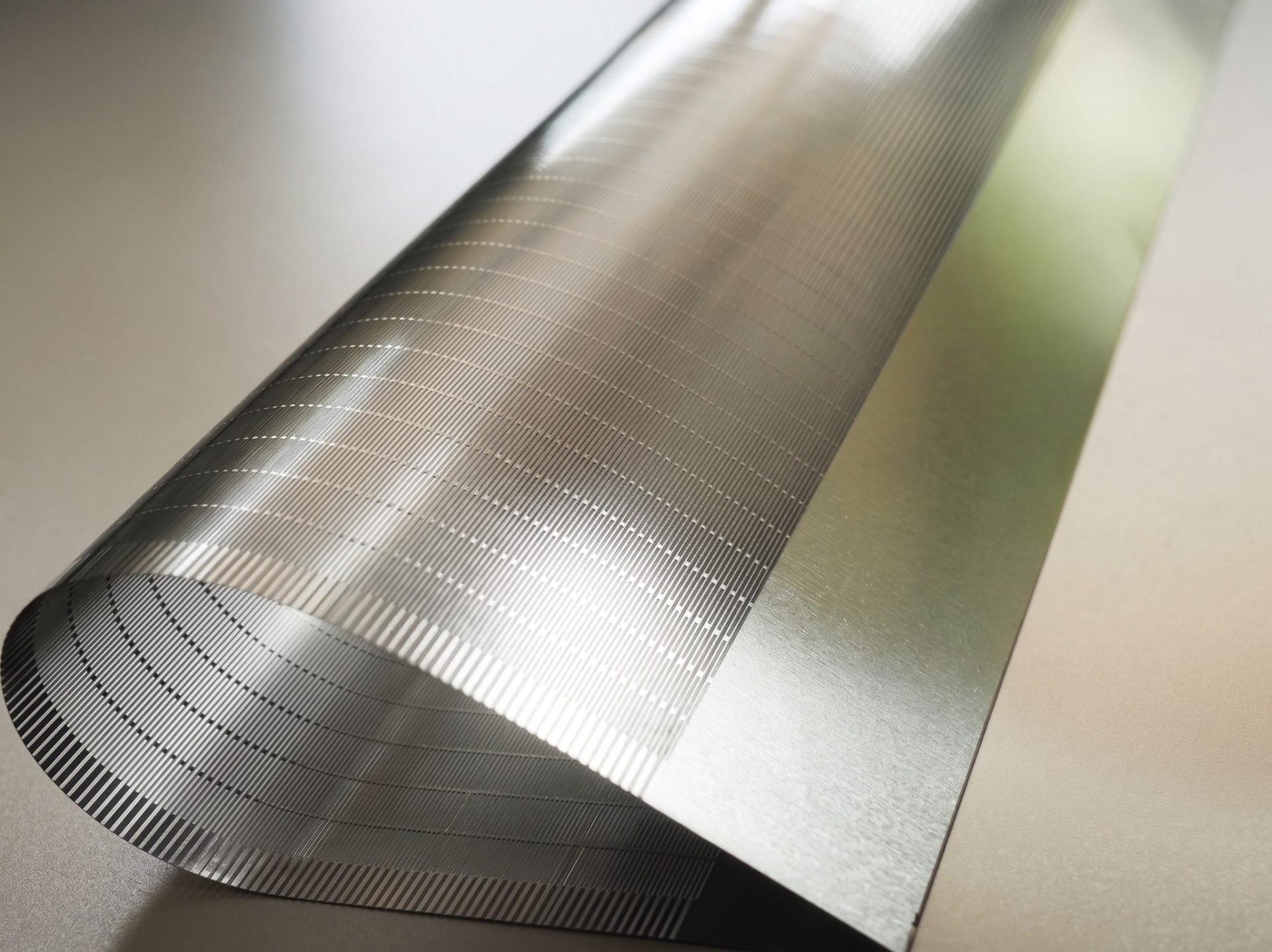 Close-up of fine etched micro-slots in a thin titanium support plate for foldable electronics